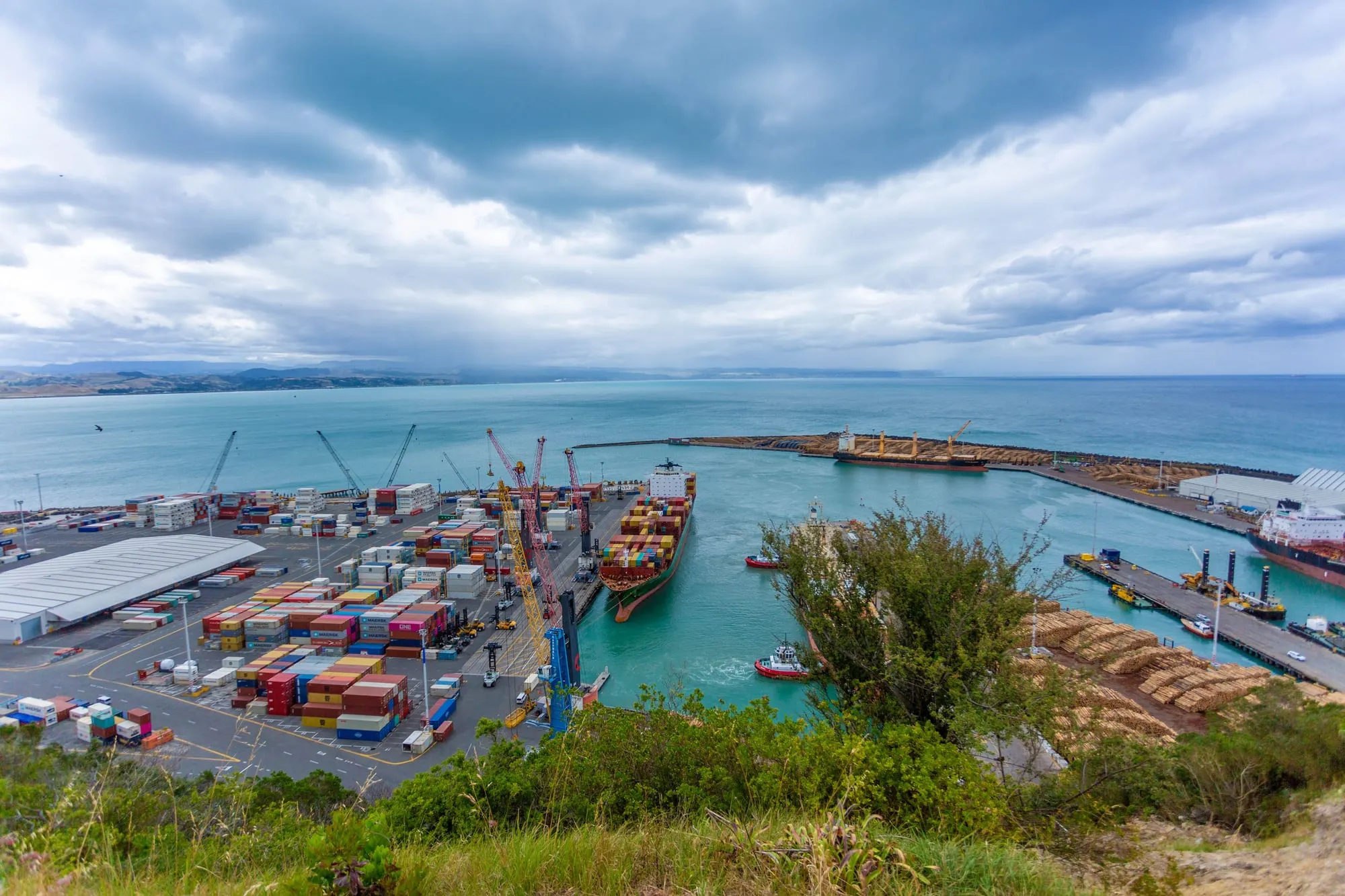 Aerial view of a container port: stacked shipping containers, cranes and a cargo ship at the quay