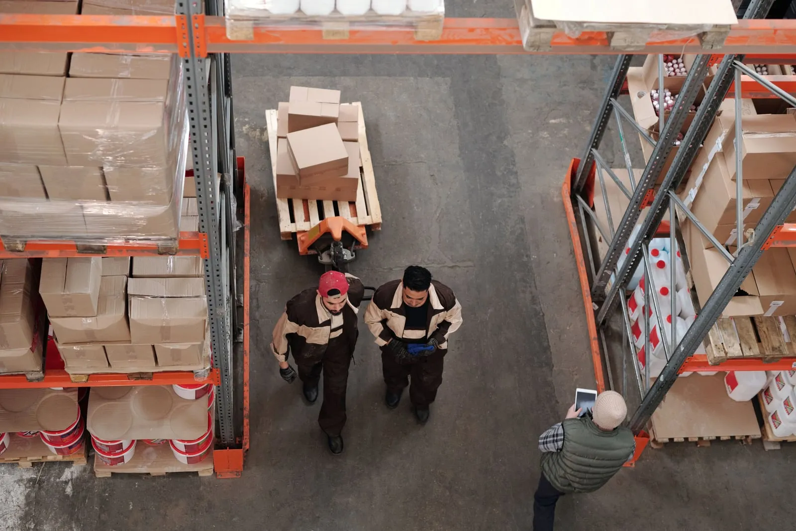 Warehouse workers seen from above moving a pallet of boxes between racks